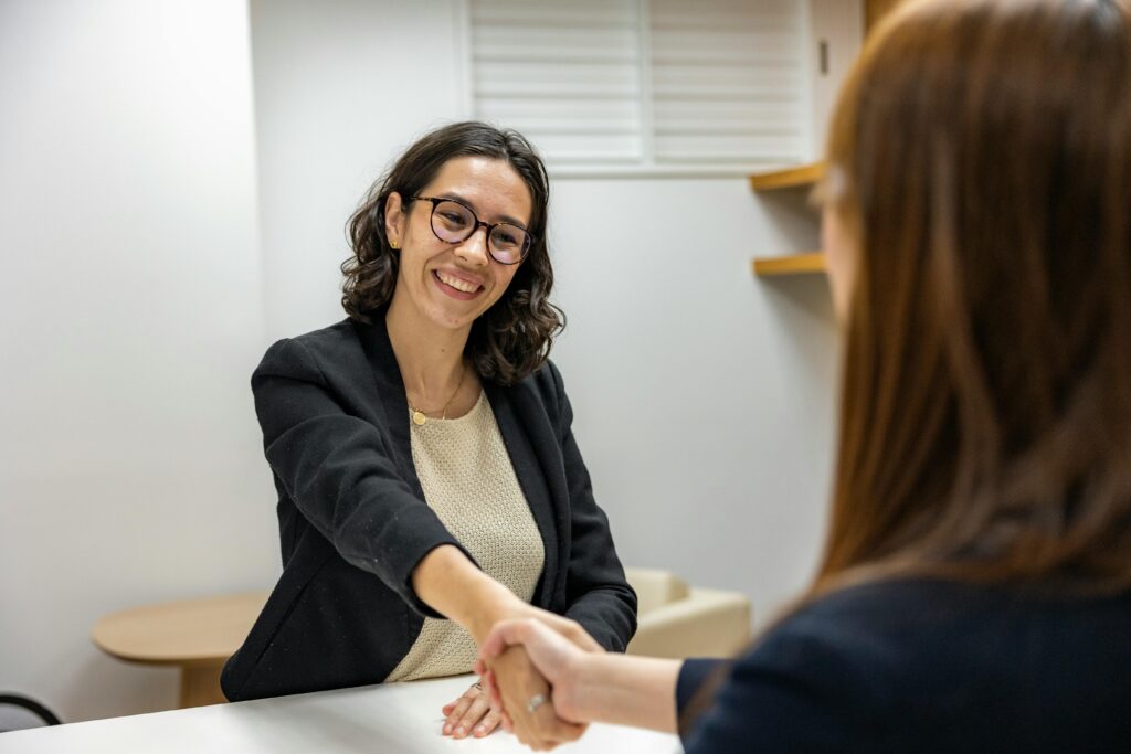 Businesswomen shaking hands in an office, representing a successful job interview or partnership.